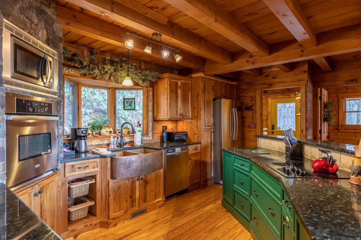 A bright, inviting kitchen with a striking green island, granite countertops, stainless steel appliances, and large windows letting in natural light. The layout encourages both cooking and casual gathering, with ample prep space and an airy feel.