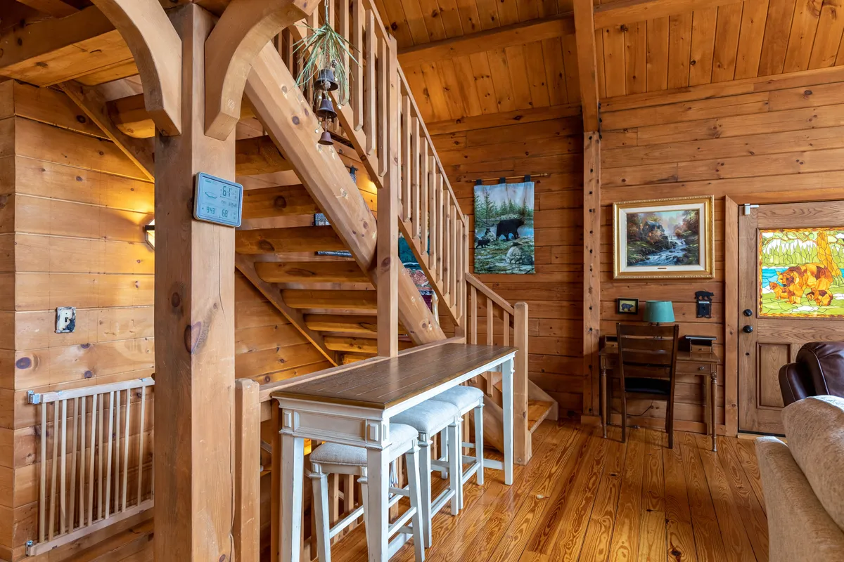 A cozy loft area with a wooden staircase, dining table, and artwork-adorned walls, bathed in natural light. The space feels welcoming and perfect for board games or casual family time.