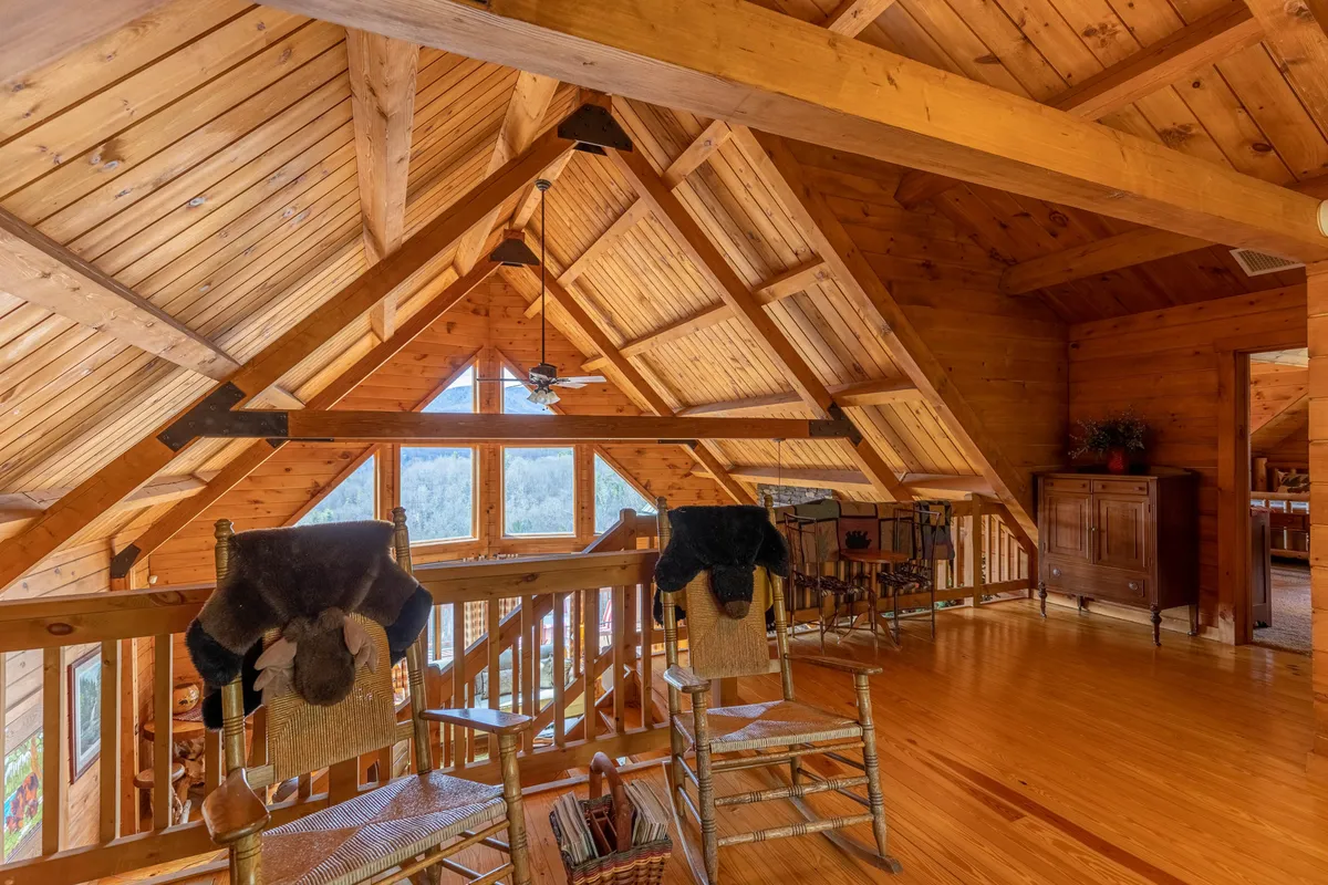 A warm, homey room with wooden beams and large windows framing beautiful views outside. Two rocking chairs are positioned perfectly to relax and take in sunsets or the shifting seasons, reinforcing the cabin’s mountain setting.