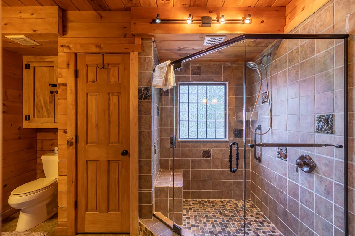 A modern bathroom with a glass shower enclosure, textured tiles, and natural wood accents. The space feels tranquil and accessible, designed for relaxation and ease of use after a day of adventure.