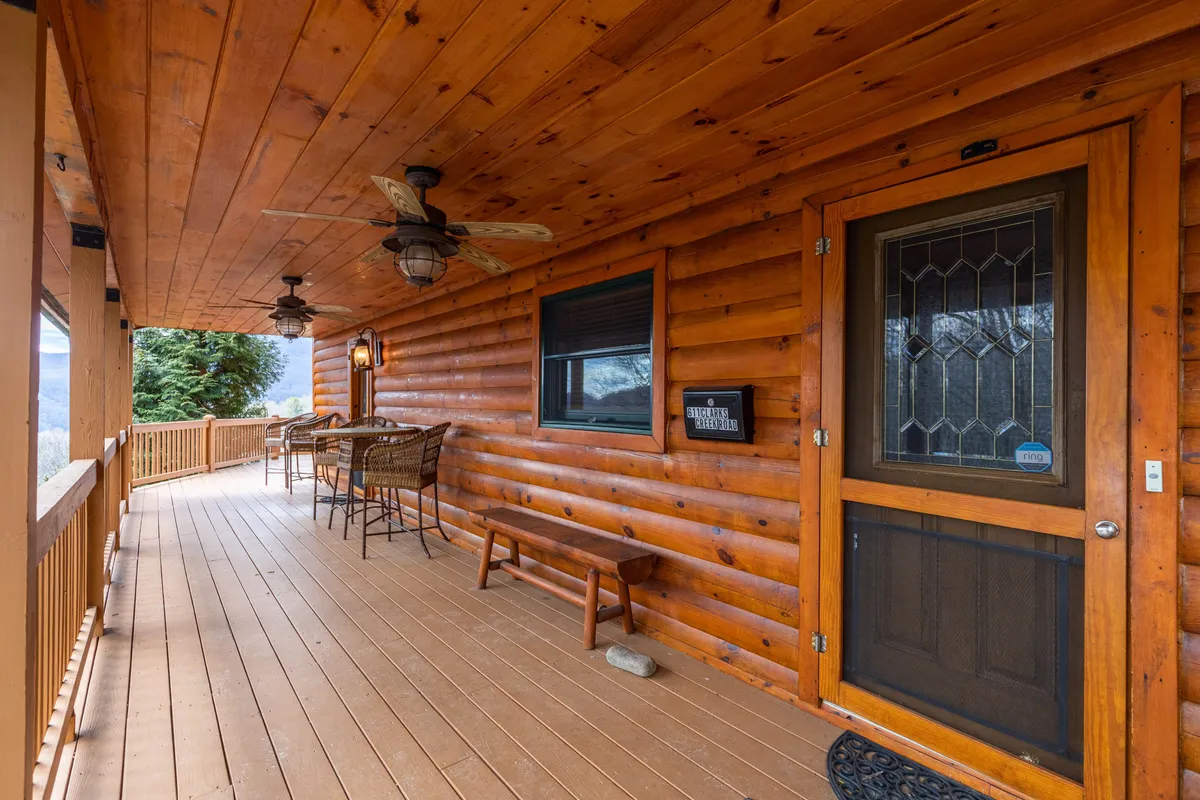 The cabin's welcoming log exterior features a cozy porch with cushioned chairs and decorative lighting. The inviting setup suggests a peaceful spot for friends to gather, chat, and share a drink while enjoying the fresh mountain air and scenic surroundings.