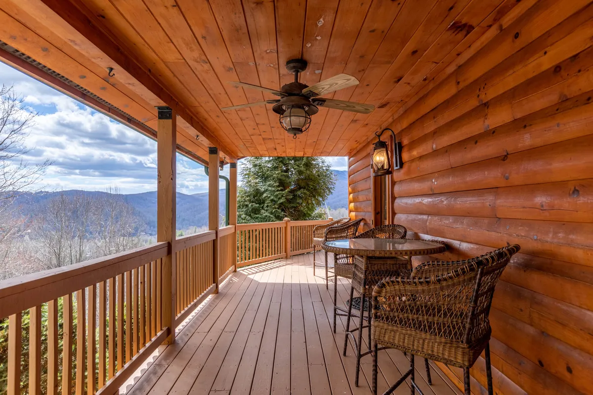 An airy outdoor seating area features wicker chairs and a round table set on a wooden deck, overlooking a panoramic mountain view. The space is ideal for morning coffee, evening chats, or stargazing with friends, providing a tranquil atmosphere to extend social time outside.