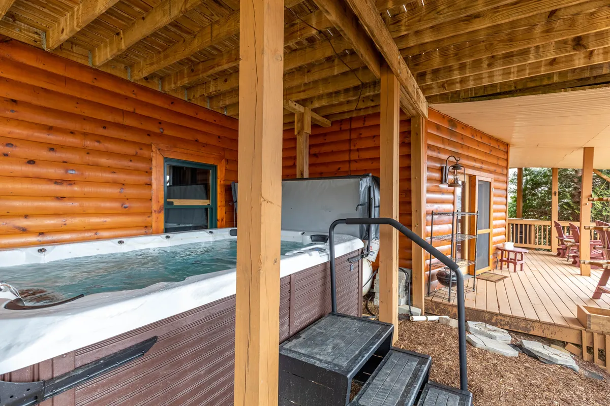 An exterior deck scene featuring a bubbling hot tub and ample outdoor space for dining and socializing, framed by rustic wooden details. The setting is inviting for sunset soaks and alfresco gatherings.