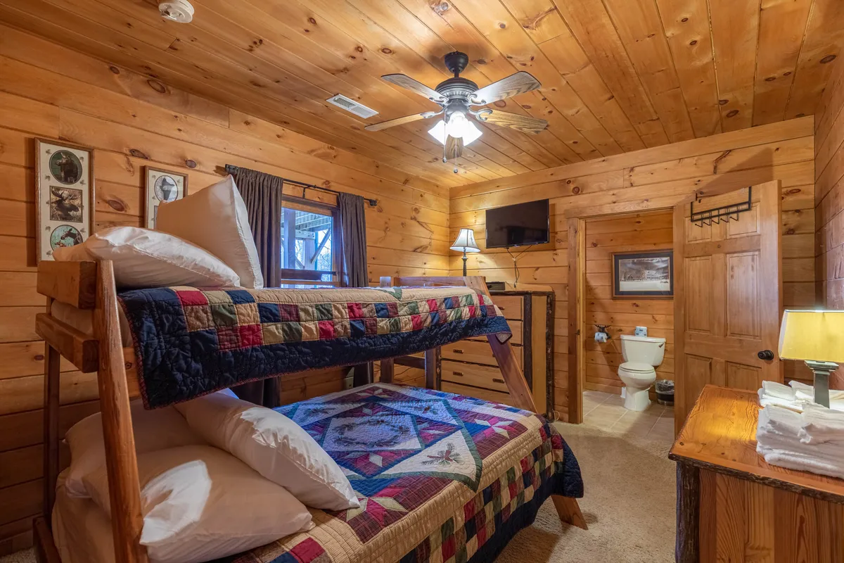 A playful bunkroom featuring sturdy wooden bunk beds with decorative quilts, a wooden dresser, ceiling fan, and cheerful wall art. The room is bright and welcoming, making it ideal for children or groups seeking a fun, private space.