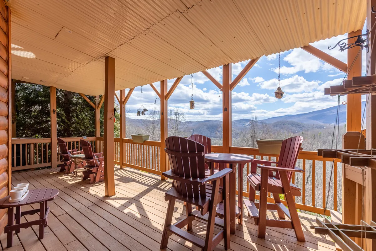 A spacious wooden deck with comfortable outdoor seating is set against a backdrop of sweeping mountain views. String lanterns add a festive, inviting touch, making the space ideal for gathering with friends to relax or enjoy a drink while soaking up the scenery.
