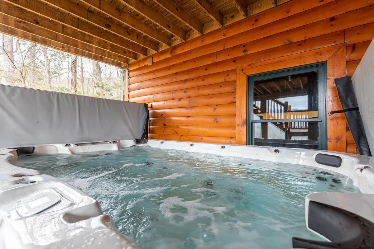 A serene indoor space with a jacuzzi, surrounded by warm wooden walls and a large window offering a picturesque view. The setup invites relaxation and socializing after a day of activities.